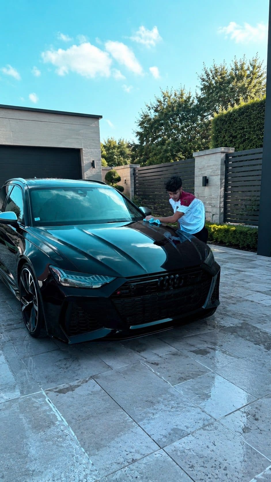 Kylian essuie le capot d'une Audi RS6 noire